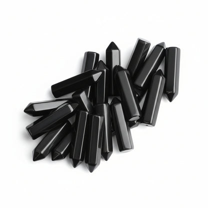 20 pieces of polished black obsidian crystal wands held in a hand, showing hexagonal points for healing and meditation.